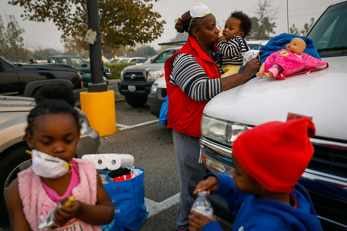 Wednesday, Nov. 14, 2018: In the smoke-filled parking lot of an emergency evacuation center in Chico, Calif., Dottie Flanders (center) holds her 9-month-old grandson, Isaiah Brooks, while her other grandchildren, London Mayo, 4 (left), and Messiha Mayo, 3, stand nearby. The family was picking up supplies after the children and their mother had to flee the Camp Fire, which destroyed most of the town where they lived, neighboring Paradise, Calif. Photo: Gabrielle Lurie