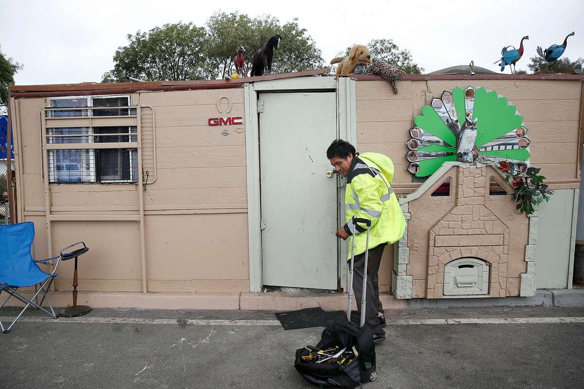 Pastor walks out the front of the structure he built and lives in along San Leandro Avenue as he heads off to his work in Oakland, CA.