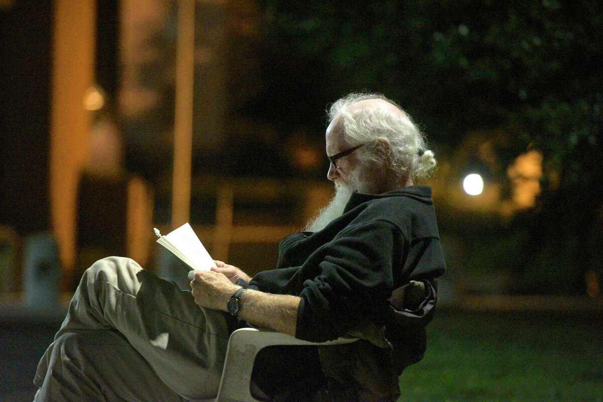 Chris Maloney, of Danbury, reads a mystery novel under a street light as he and other's that are homeless prepare to spend another night sleeping in tents in front of city hall as a to protest the closing of the Jericho shelter. Tuesday night, September 10, 2019, in Danbury, Conn.