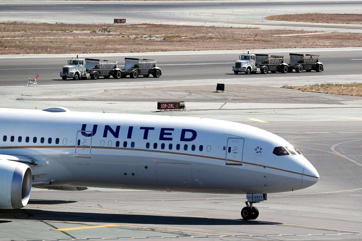 Construction trucks drive past a United plane at SFO in San Francisco, Calif., on Sunday, September 15, 2019.