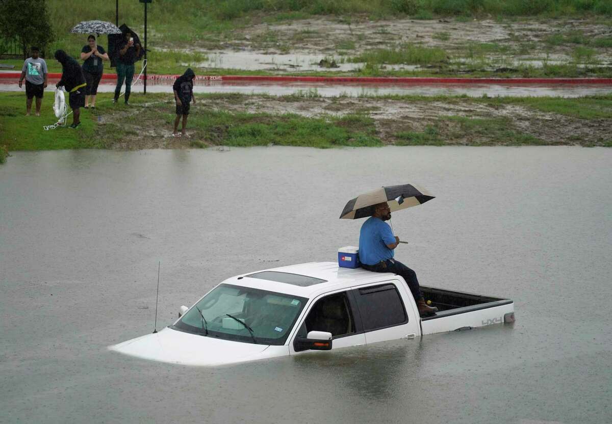 A man sits on top of a truck on the flooded feeder road along Sam Houston Tollway West between Wilson and Ralston Rd. near Garners Bayou while people try to toss him a life preserver ring Thursday, Sept. 19, 2019, in Houston. Members of the Houston Fire Dept. brought him a life jacket and walked him to dry land.