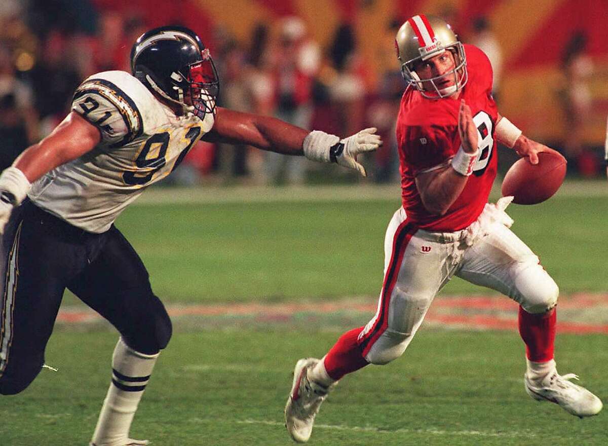 MIAMI, : San Francisco 49ers quarterback Steve Young (R) evades the grip of San Diego Chargers Leslie O'Neal, 29 January 1995 during the third quarter of Super Bowl XXIX in Miami. Young has throw for a record six touchdowns during the game. The 49ers lead the Chargers 49-18 in the fourth quarter. (COLOR KEY: Young red jersey) AFP PHOTO (Photo credit should read JEFF HAYNES/AFP/Getty Images)