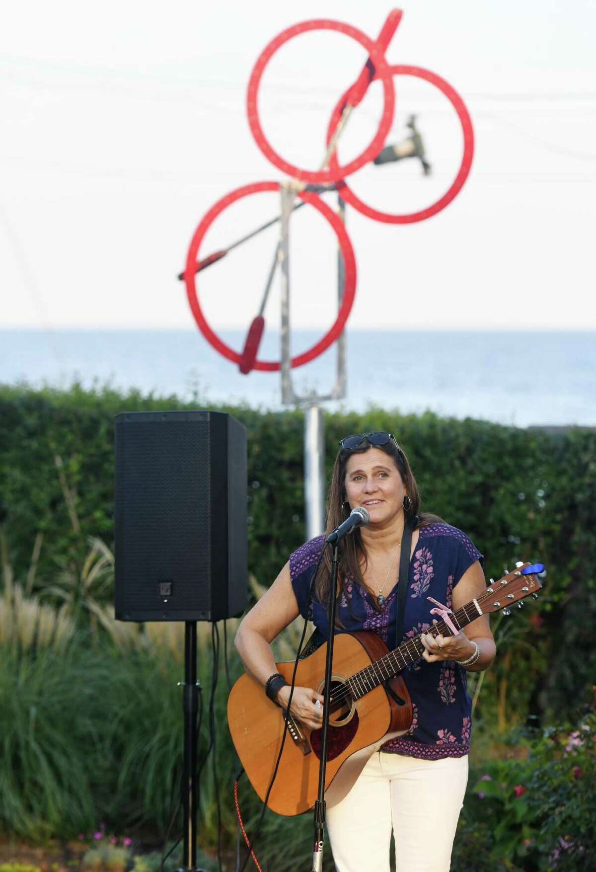 Lizzie Swan performs a song by Warren Zevon during the "Three Souls" wind sculpture dedication at the home of Steve Loeb at the end of Shippan Avenue in Stamford, Conn. Sunday, Sept. 22, 2019. Loeb purchased the land on Shippan Point where Madonna Badger's house burned down in 2011, killing her parents and three daughters and dedicated the wind sculpture in honor of the three young children killed in the fire. It has one ring for Lily Badger, who was 9 when she died, and two smaller rings for her twin sisters, Grace and Sarah, who were 7. The ceremony was attended by about 100 neighbors and friends as Loeb recalled memories of his son playing with the children in the house next door. Rabbi Debra Salomon and musician Lizzie Swan said a prayer and performed a song for the crowd that culminated in everybody putting their arms around their neighbors.