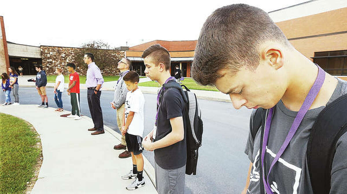 Civic Memorial High School sophomore Peyton Keller, right, bows his head during prayers around the flag pole in front of the Bethalto high school Wednesday morning.