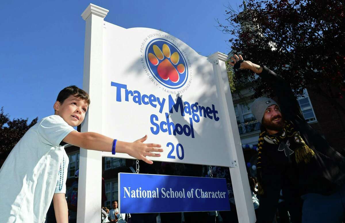 Tracey Elementary School 4th grader Jaxon Casey and his dad, Zachary Casey, pose by the new sign as the schools holds its official Character Education Magnet Kick-Off Celebration on Friday, September 27, 2019, in Norwalk, Conn. The school celebrates not only last year’s accomplishment of becoming a State School of Character, but a National School of Character as well. Tracey will now be known as Tracey Magnet School, a recognized National Blue Ribbon School.