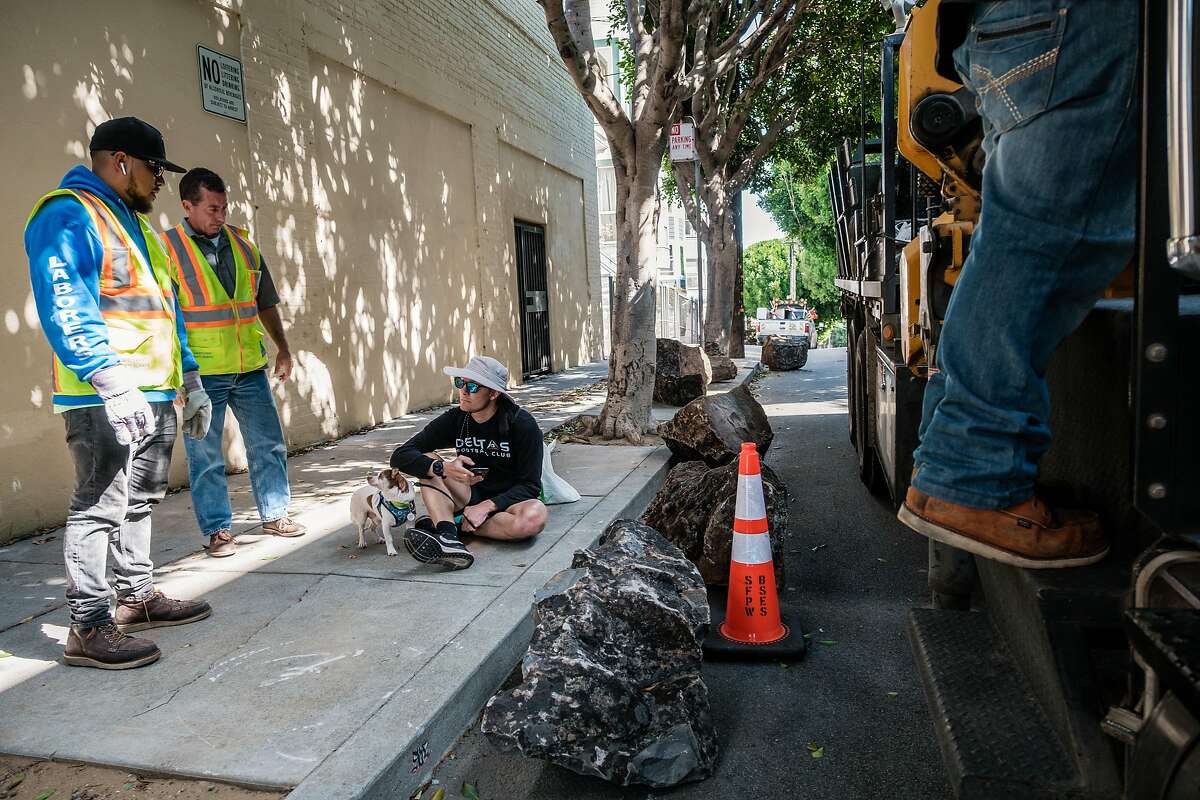 City workers speak to a man unidentified man who refused to move so they could lift boulders back onto to the sidewalk after they were moved from the sidewalk to the street in San Francisco, Calif. on Saturday, September 28, 2019. The boulders are meant to deter homeless encampments on the sidewalk.