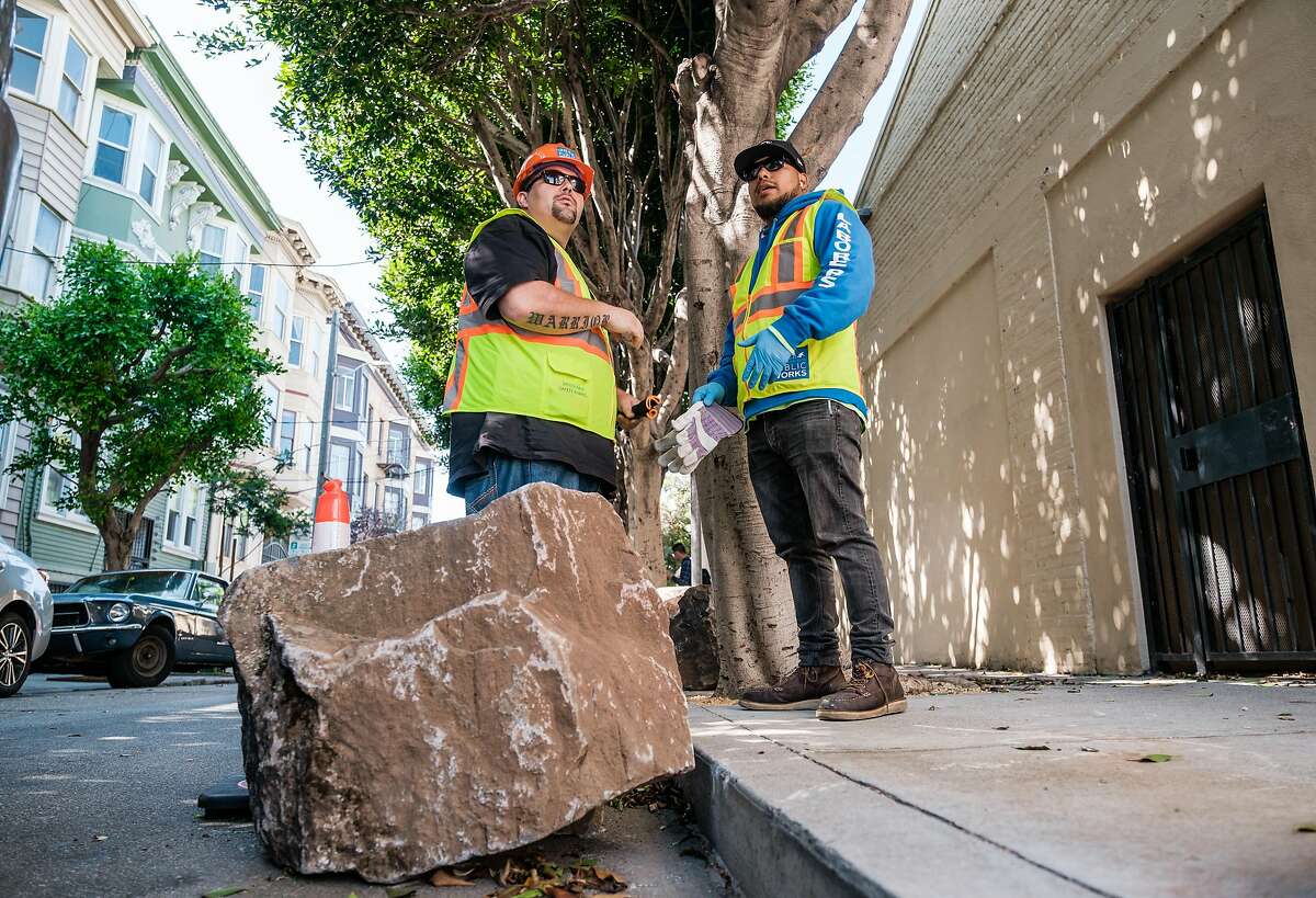 City workers prepare to lift boulders back onto to the sidewalk after they were moved to the street, in San Francisco on September 28, 2019. The boulders are meant to deter homeless encampments on the sidewalk.