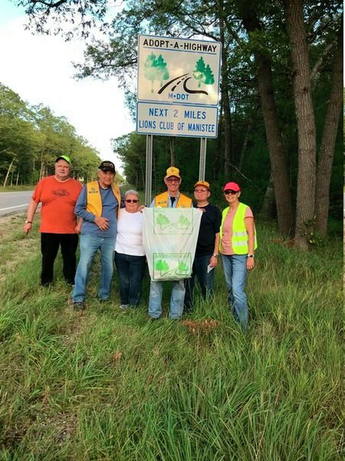 Manistee Lions Club members pose for a photo by a sign following their highway clean up. (Courtesy Photo/Susan Meyers)