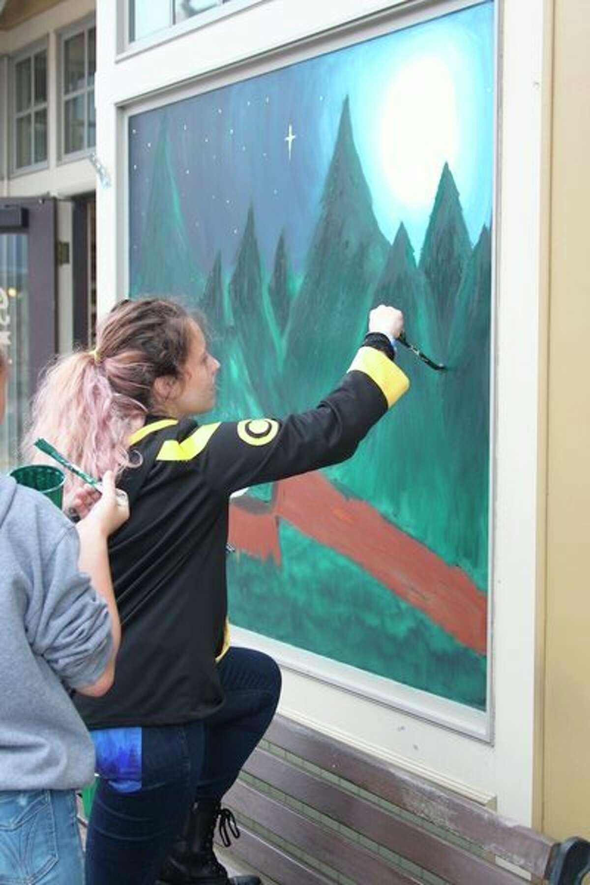 Freshmen class members put the final touch on their mural on the window at Snyder Shoes. (Ken Grabowski/News Advocate)