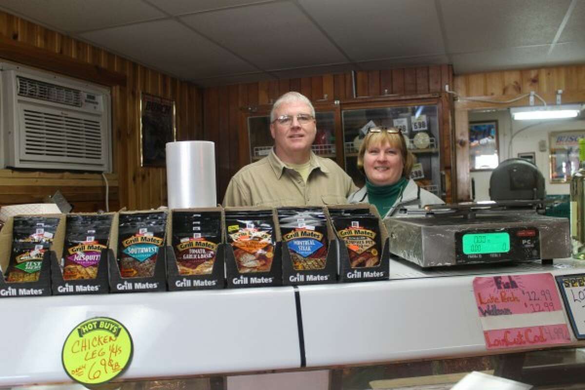 Jim Tighe and Merrill Tighe, owners of the M-55 Market in Wellston, stand behind the meat counter 30 years after posing for the same photo when they first took over the store on March 1, 1985. (Justine McGuire/News Advocate)