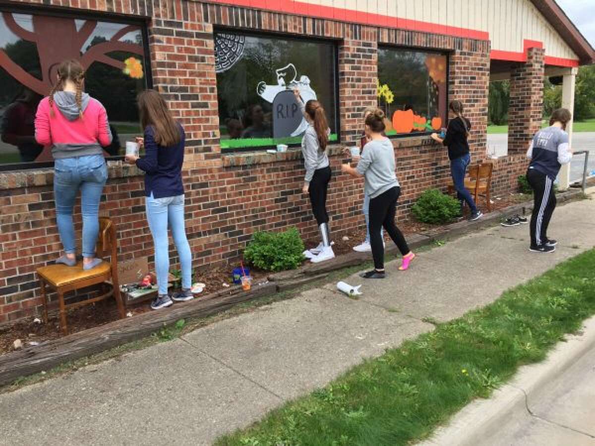 Onekama High School art students paint the windows of the former Saco’s Market, soon-to-be the EZ Market.