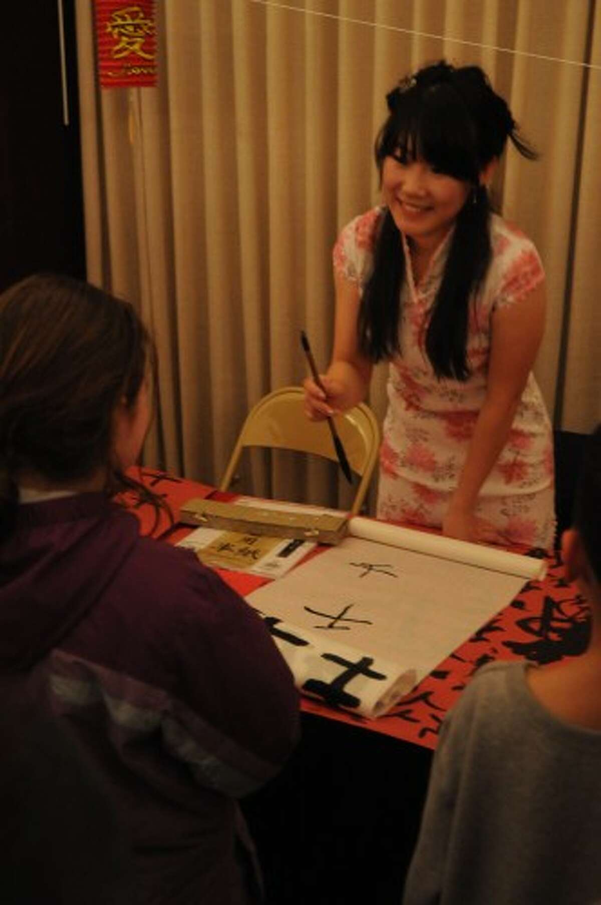 DEMONSTRATION: Chinese Cultural Student Group chair Xiao Hua works a table on Tuesday at the university’s Chinese New Year celebration. Attendees of the celebration visited the tables to learn about Chinese culture and Asian religions. Here, children practiced writing Chinese characters. (Pioneer photo/Kyle Leppek)