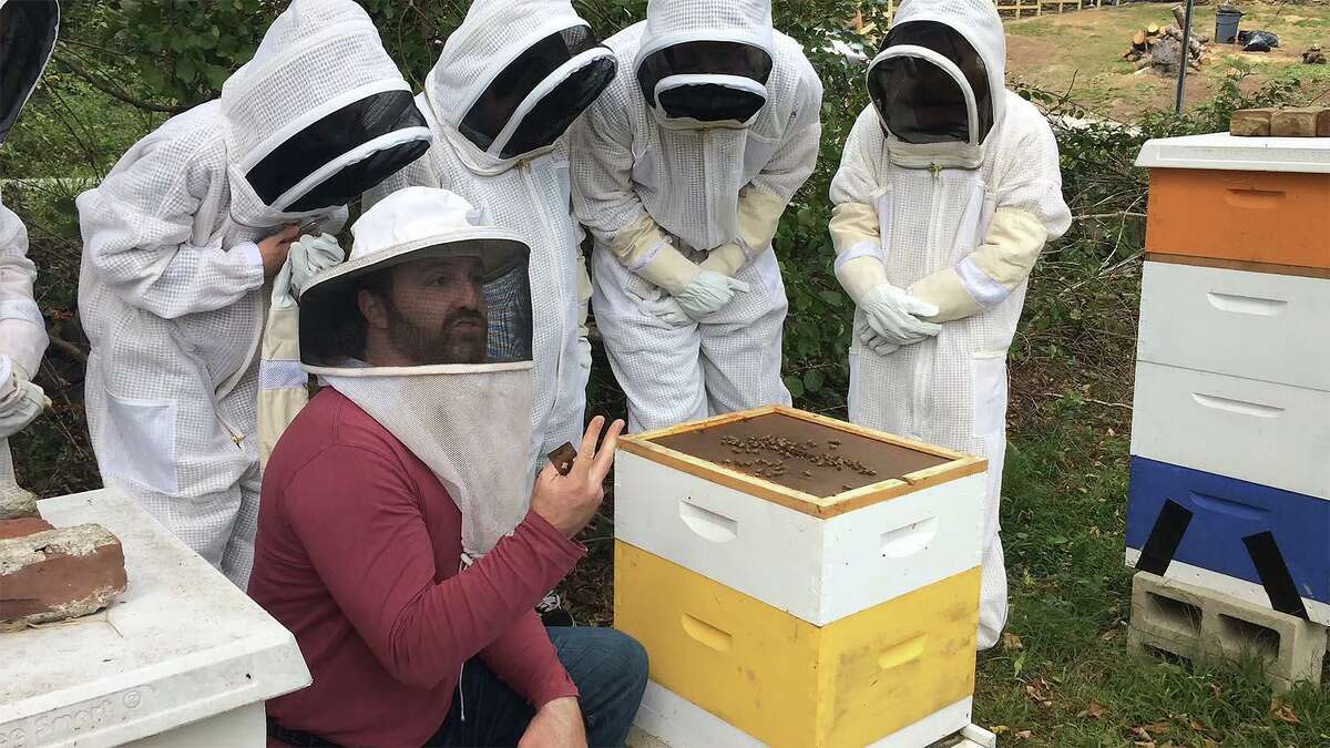 Drew Burnett, kneeling, at right, gave Wesleyan students a tour of a local apiary, where they learned about the centrality of honeybees to our industrialized agricultural system. The students are pictured holding Drew’s Honeybees lip balm.