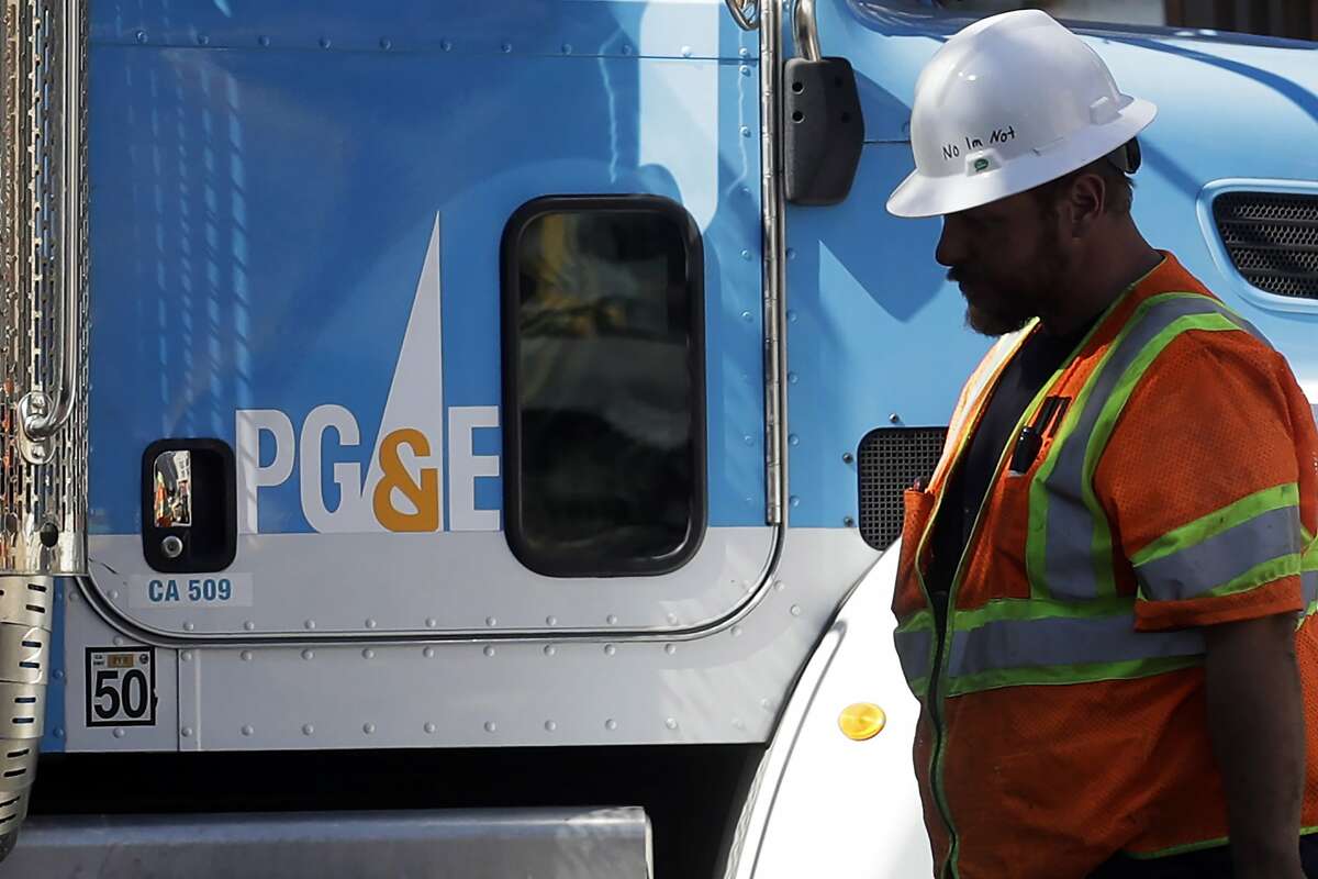 In this Thursday, Aug. 15, 2019 photo, a Pacific Gas & Electric worker walks in front of a truck in San Francisco. San Francisco officials are offering to buy Pacific Gas & Electric's power lines and other infrastructure in the city for $2.5 billion. Mayor London Breed and City Attorney Dennis Herrera presented the offer in a letter sent to the utility Friday, Sept. 6, 2019. (AP Photo/Jeff Chiu)