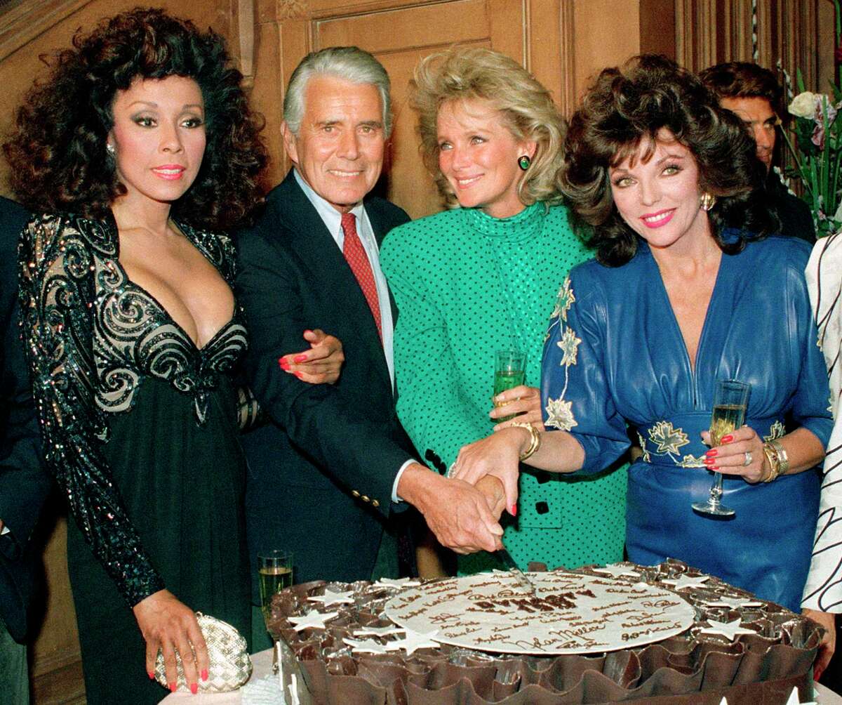 FILE - This Sept. 24, 1986 file photo shows, Diahann Carroll, John Forsythe, Linda Evans and Joan Collins from "Dynasty" cutting a cake to commemorate the production of 150 episodes of the show in Los Angeles. Carroll died, Friday, Oct. 4, 2019, at her home in Los Angeles after a long bout with cancer. She was 84. (AP Photo/Reed Saxon, File)