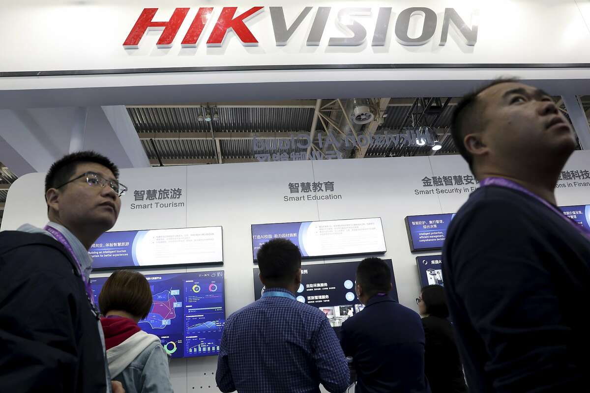 FILE - In this Tuesday, Oct. 23, 2018, file photo, visitors pass by a booth for state-owned surveillance equipment manufacturer Hikvision at the Security China 2018 expo in Beijing, China. The United States is blacklisting a group of Chinese tech companies that develop facial recognition and other artificial intelligence technology that the U.S. says is being used to repress China’s Muslim minority groups. The blacklisted companies include Hikvision, a global provider of video surveillance technology. (AP Photo/Ng Han Guan, File)