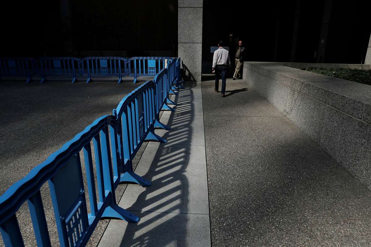 A pedestrian walks by barricades in front of the PG&E's building at 77 Beale Street in San Francisco, Calif., on Wednesday, October 9, 2019. The utility’s personnel there manage the public safety power shutoffs, which began last night and will continue throughout the day today as the Diablo winds begin to rise.