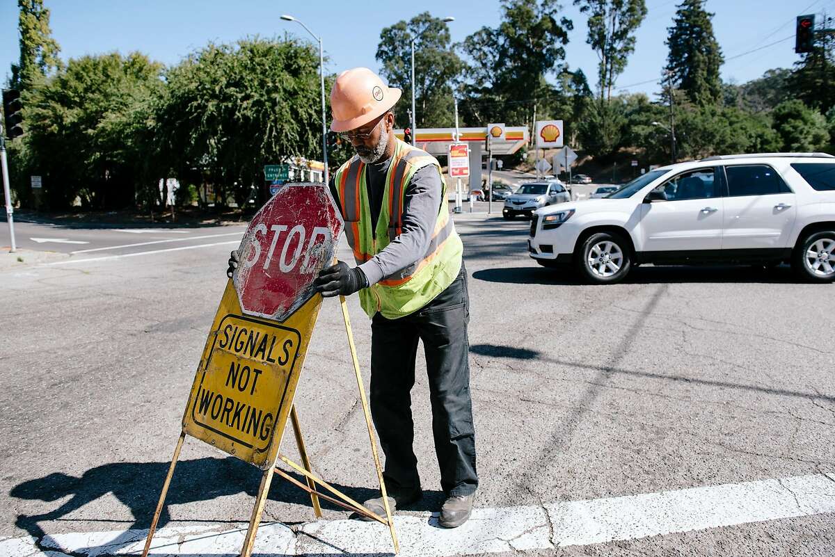 Tyrone Rowe with the Oakland Department of Transportation sets out stop signs at the corned fo Golf Links Road and 98th Avenue after preemptively setting the traffic lights to flashing red in lieu of scheduled power outages in Oakland, California, on Friday, Oct. 9, 2019.