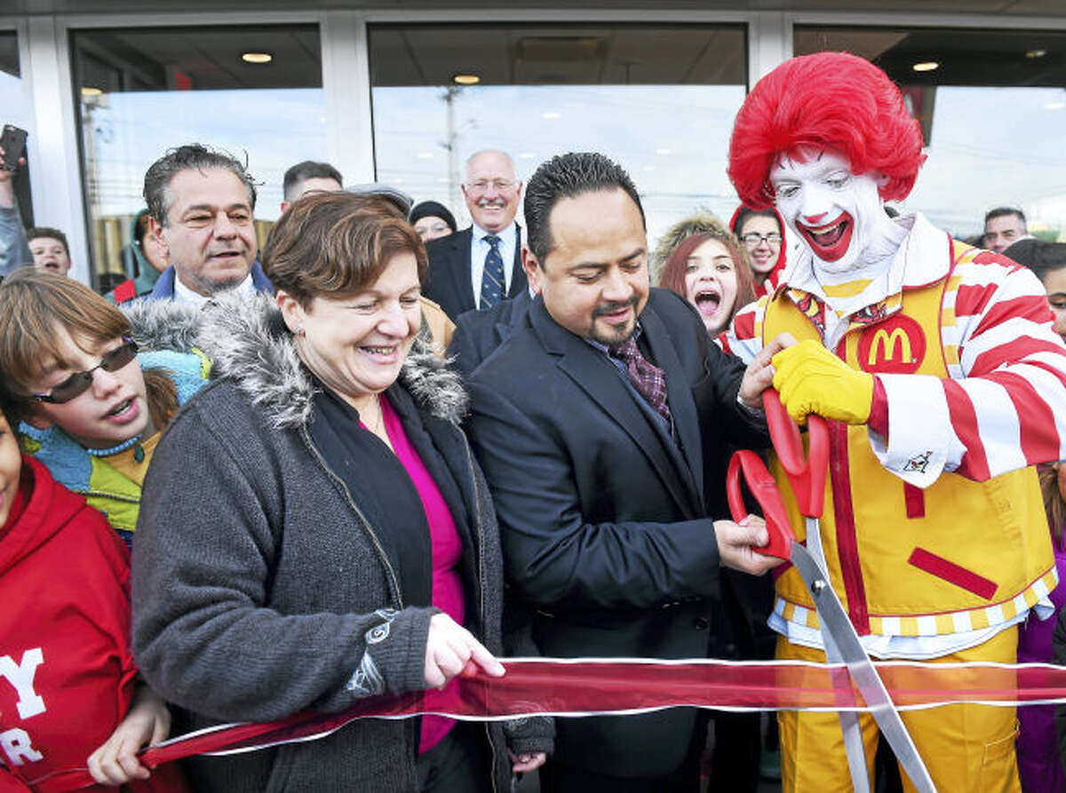 Left to right, Derby Mayor Anita Dugatto, McDonald’s owner/operator Joe Rodriguez and Ronald McDonald cut a ribbon for the grand re-opening of McDonald’s on Division Street in Derby on Dec. 19. In the background at left is Ansonia Mayor David Cassetti.