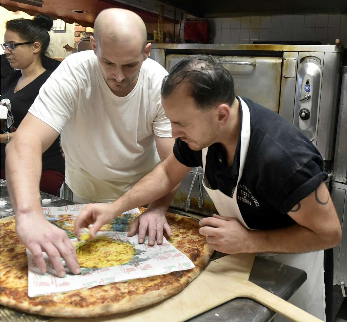 Pizza maker Chris Stackpole, left, and his boss Donato Cappetta, owner of Cappetta's Italian Imports, Pizza and Catering in West Haven, make a giant, 30-inch round pizza with an eatable blue-and-gold ribbon on top to honor nearby Forest School for being named as just one of four national Blue Ribbon Schools in Connecticut.