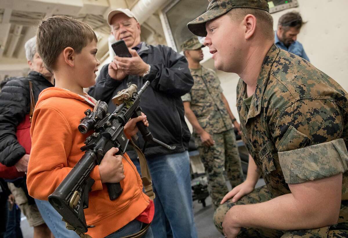 US Marine Matthew Hulslander (right) lets Luke D'Urso, 7, hold an M4 machine gun during a tour aboard the USS Somerset naval warship during Fleet Week festivities in San Francisco, Calif. Saturday, Oct. 12, 2019.