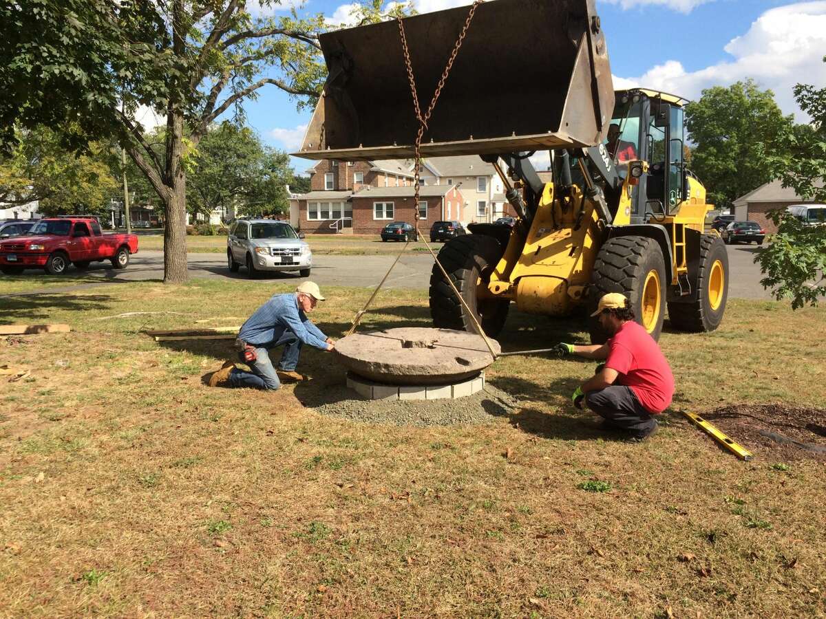 Photo by Lynn Fredricksen Walt Brockett, a member of the North Haven Historical Society and Museums, directs town employees as he positions an old millstone that he has repurposed as a bench. Both the sandstone and the granite millstones have been installed on the lawn between the Cultural Center and the library.