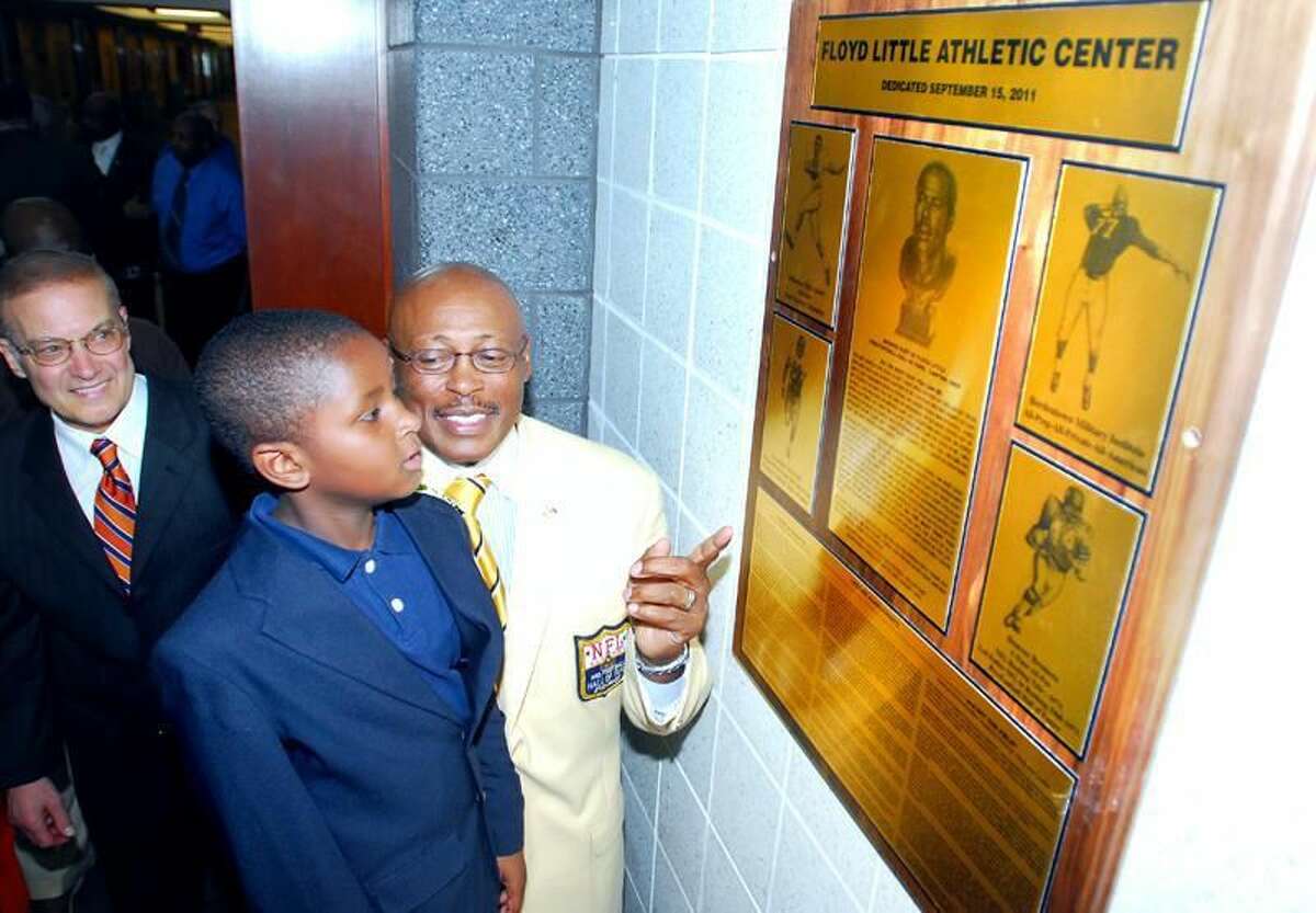 Photo by Arnold Gold/Register Bill Santillo, left, chairman of the dedication committee, watches football legend Floyd Little, right, show his grandson, Blaze Kennedy Jones, 6, the plaques honoring Little during the renaming of the New Haven Athletic Center the Floyd Little Athletic Center Thursday in New Haven.