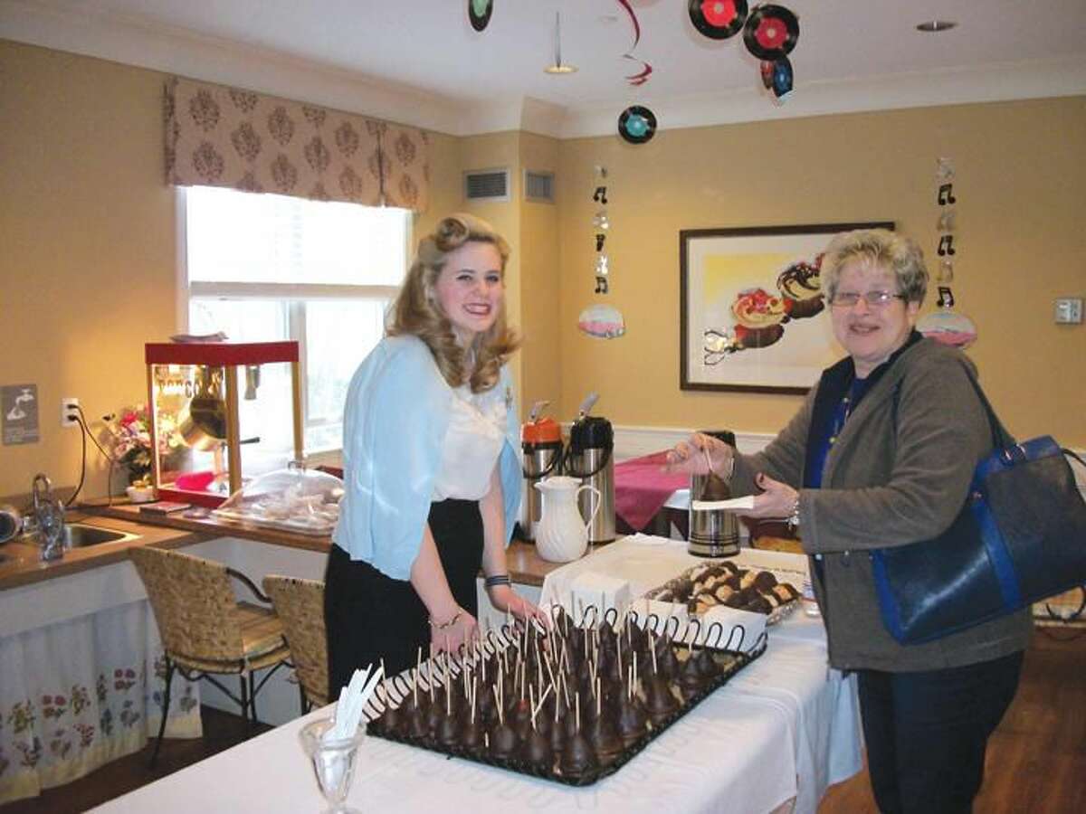 Photo By Lynn Fredricksen Dressed in a vintage 1950s outfit, Kate Taylor, a server at Maple Woods, serves up a chocolate covered strawberry on a stick to Josephine Marra. The two were at a fundraising event to benefit the Hamden Senior Wish Society held recently at Maple Woods.
