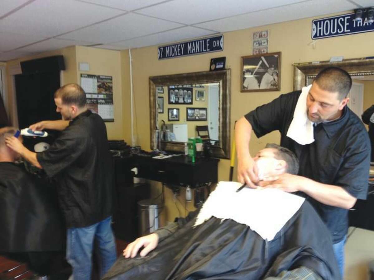Photo by Lynn Fredricksen Rob Palmieri gives his friend, Michael Nazario, of North Haven, one of his specialty “Cut Throat Shaves” at Palmieri’s shop, Figoro’s Barber Shop at 3820 Whitney Ave. in Hamden. In the background, barber Brandon Nalle, gives Joe Chauncy a trim.