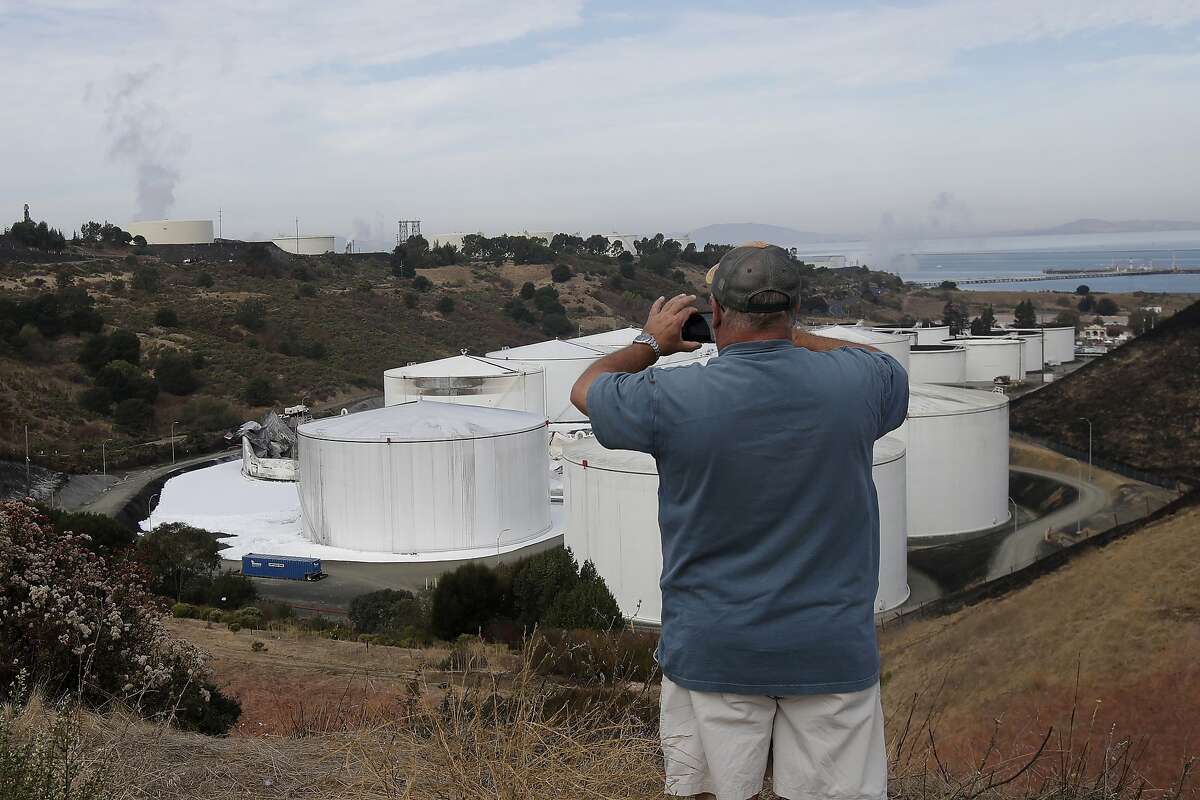 Mark Storey takes photos of damage from a Tuesday, Oct. 15, 2019, fire at NuStar Energy fuel storage facility in Crockett, Calif., Wednesday, Oct. 16, 2019. Officials were trying to determine Wednesday if a 4.5 magnitude earthquake triggered an explosion at a fuel storage facility in the San Francisco Bay Area that started a fire and trapped thousands in their homes for hours because of potentially unhealthy air. (AP Photo/Jeff Chiu)