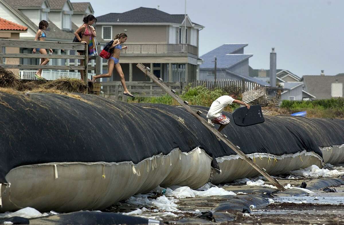 Pedestrians climb over an exposed geotube in Galveston, Texas, in this July 18, 2003, file photo, as they head to the beach. The large sand-filled tubes were placed under sand dunes in 1999 to protect the beach from erosion. The geotubes were exposed when Hurricane Claudette caused erosion and beach house damage up to 120 miles up the coast from landfall.