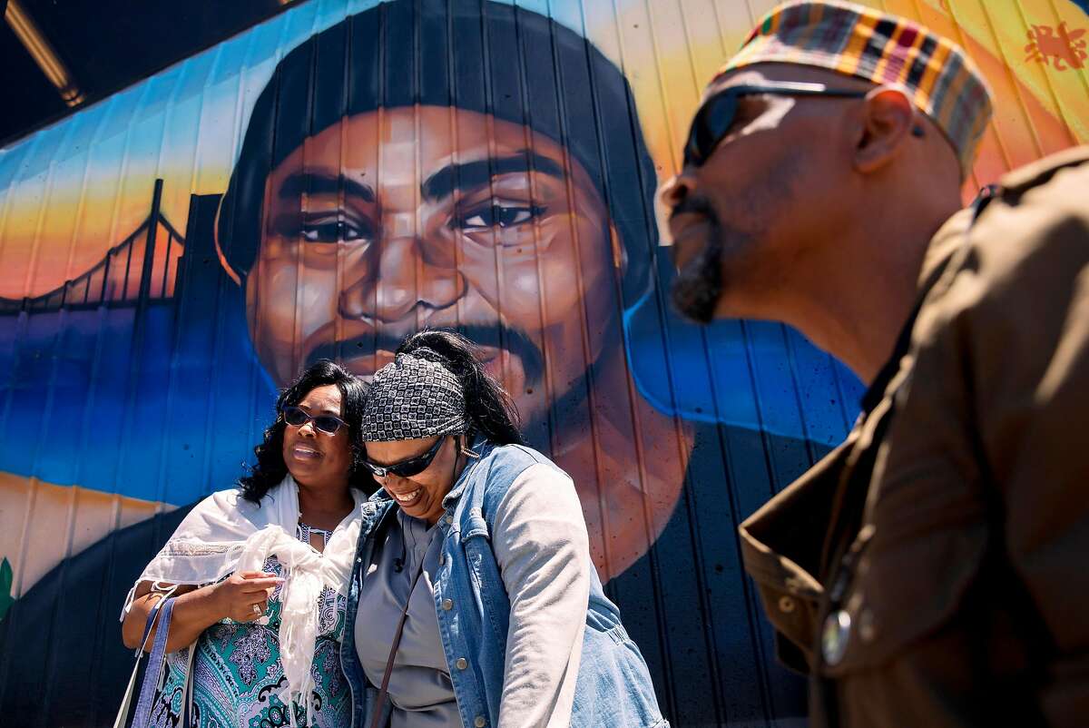 Wanda Johnson (left), mother of the late Oscar Grant, greets a friend while standing underneath a large mural honoring her son during a mural and street naming unveiling for Oscar Grant at Fruitvale BART Station in Oakland, Calif. Saturday, June 8, 2019.
