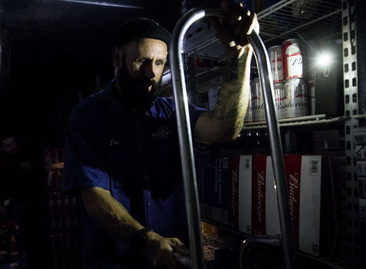 Beer distributor Joe Wheeler restocks beer by the flashlight of a cell phone at La Tapatia Market in Napa, Calif. Wednesday, Oct. 9, 2019 following the first stage of PG&E Public Safety Power Shutoffs across Northern California.