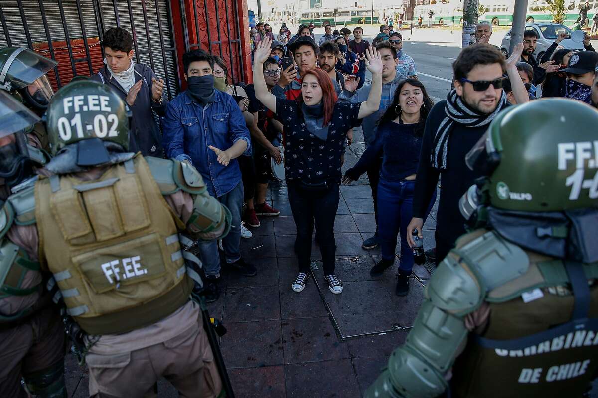 Riot police stand next todemonstrators during protests in Valparaiso, Chile, on October 20, 2019. - Fresh clashes broke out in Chile's capital Santiago on Sunday after two people died when a supermarket was torched overnight as violent protests sparked by anger over economic conditions and social inequality raged into a third day. (Photo by JAVIER TORRES / AFP) (Photo by JAVIER TORRES/AFP via Getty Images)