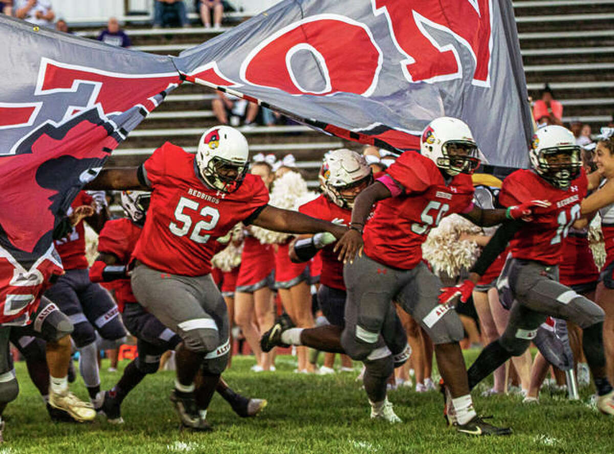 Alton’s Kahron Edwards (52), Ihzel Brown and Alero Watson (10) bust through the banner to lead the Redbirds onto the field at Public School Stadium before a Sept. 13 game vs. Collinsville in Alton. The 3-5 Redbirds are back home Friday to end their season against DeKalb.