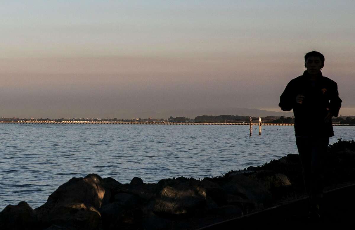 Smoke from the northern Sonoma County Kincade Fire is seen in the North Bay as a person jogs along the waterfront in Emeryville, Calif. Friday, Oct. 25, 2019.