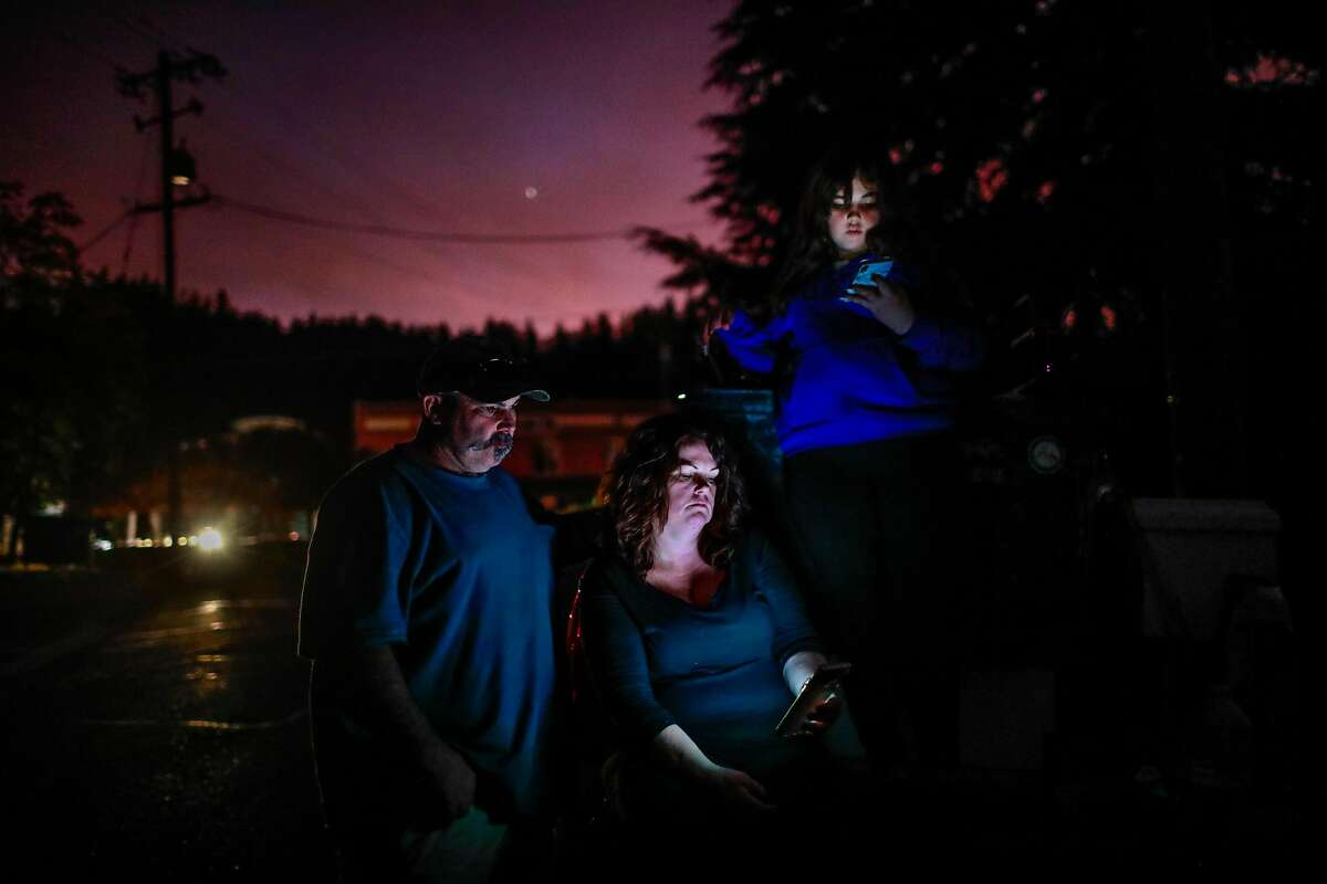 (l-r) Aaron Johnson, wife Tammy White and daughter Leah Johnson, 11, sit outside their house without electricity as they watch the news on their phone for updates about the nearby Kincade Fire in Geyserville, California, on Thursday, Oct. 24, 2019. Leah said, "I'm just scared our house is going to burn if it jumps over the river".