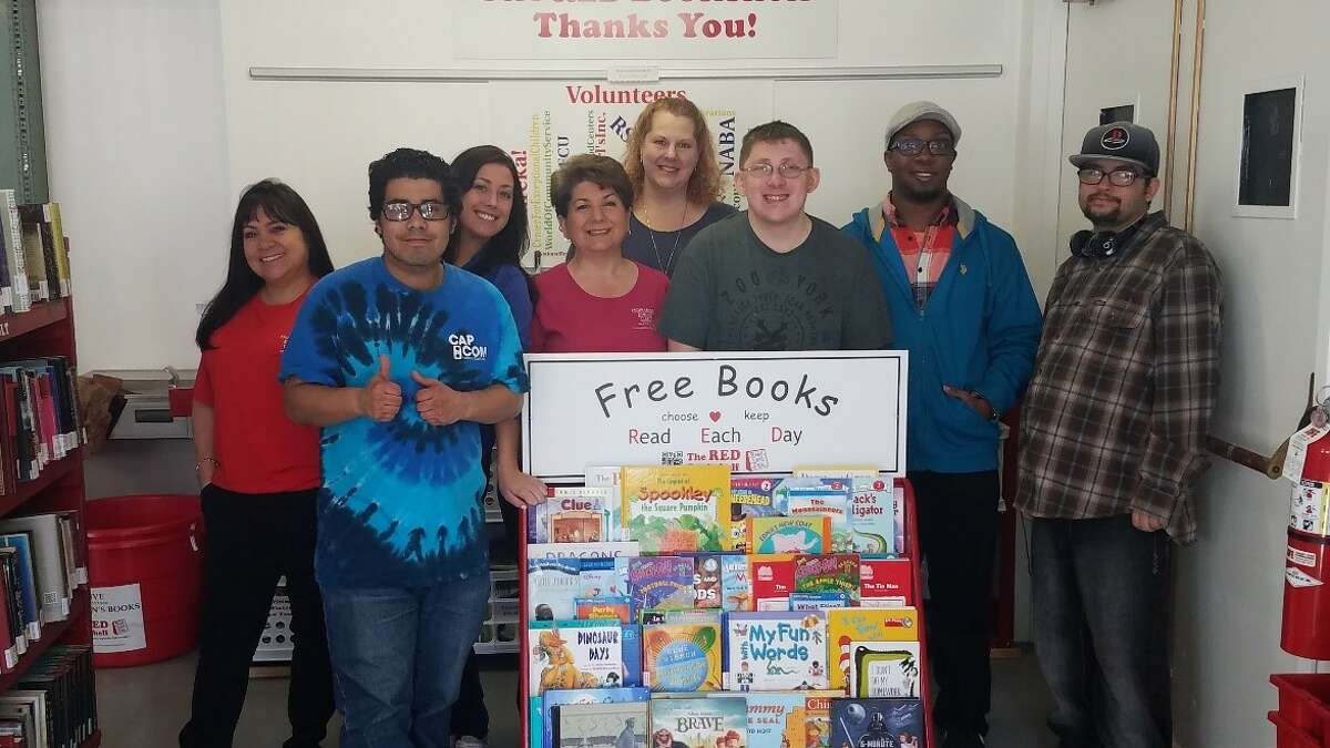 Volunteers stand in front of a RED Bookshelf, which has a variety of free children's books and can be found in waiting rooms and doctors offices.