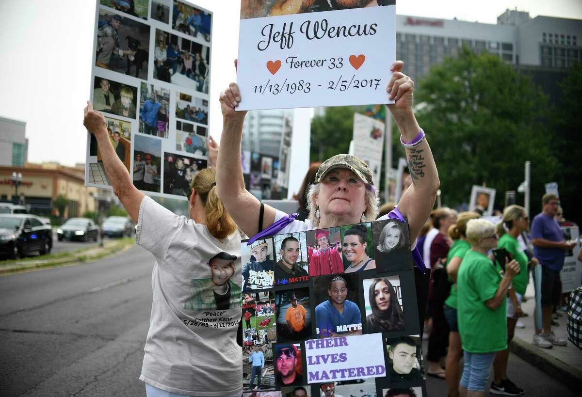 Lynn Wencus of Wrentham, Mass., holds a sign with a picture of her son Jeff and wears a sign of others' loved ones who have died from opioid overdoses, during a protest on Aug. 17, 2018, at Purdue Pharma’s headquarters in downtown Stamford, Conn.