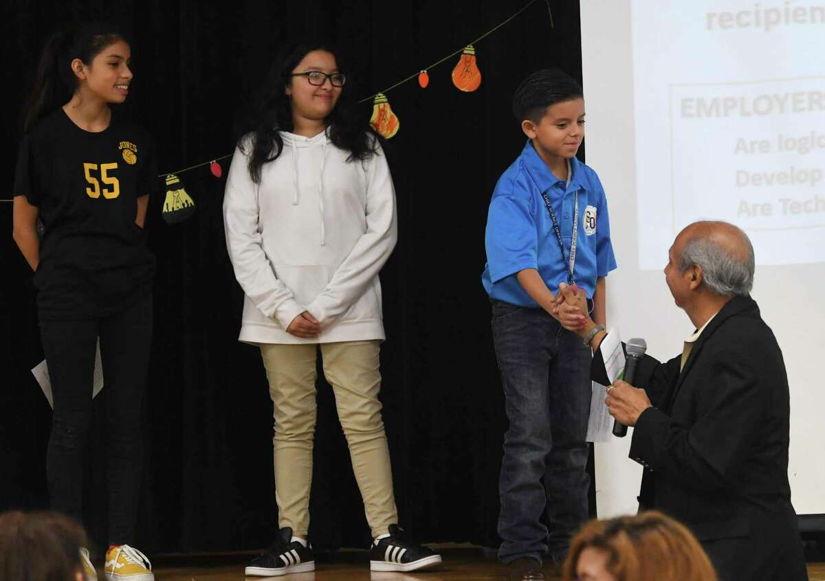 Emily Martinez, left, Abigail Sanchez and Damien Gauna, who are chief science officers at Anson Jones Middle School, are greeted by STEM education consultant Rudy Reyna during the Lights ON! STEM Spooky Family Fair on Thursday.