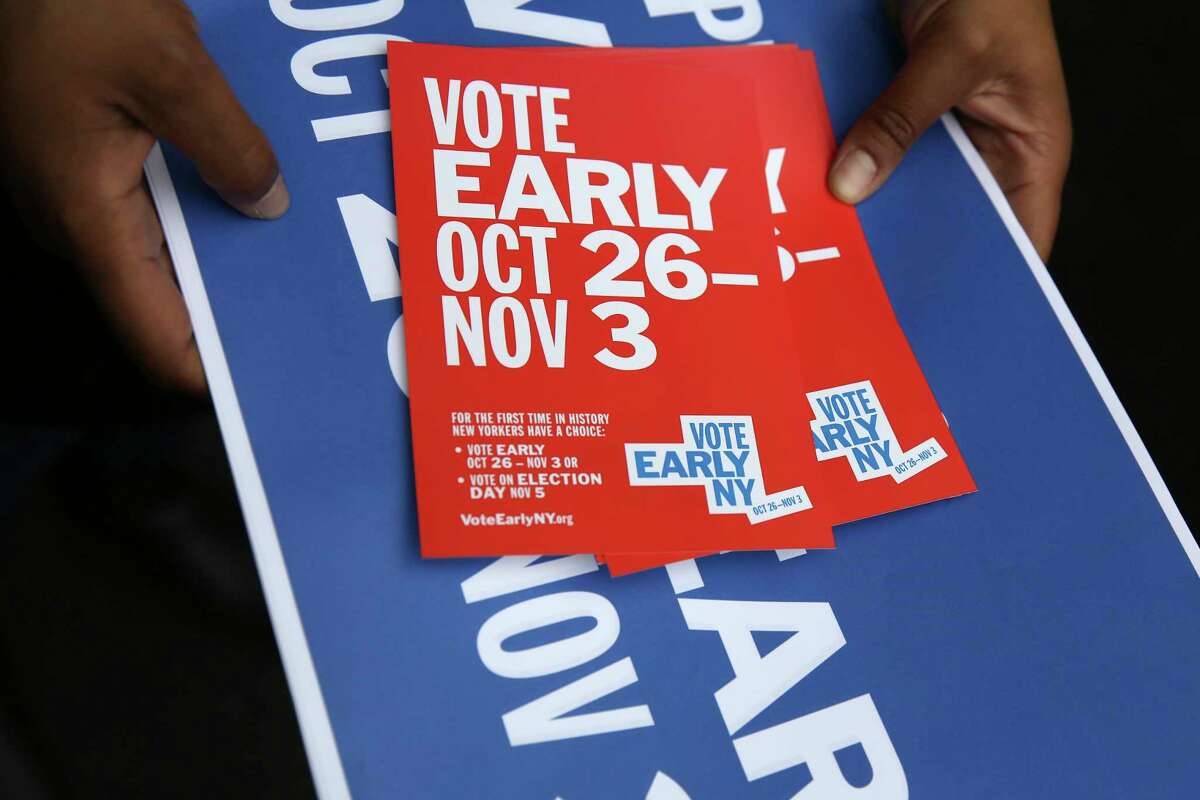 A woman hands out postcards and posters with information about early voting at a rally in New York, Tuesday, Oct. 22, 2019. Early voting is set to happen for the first time in New York, and advocates hope the benefits of expanded ballot box access will outweigh the cost and headaches of keeping the polls open for more than a single day. Starting Saturday, voters in this autumn's election can cast ballots at select polling locations through Nov. 3. (AP Photo/Seth Wenig)