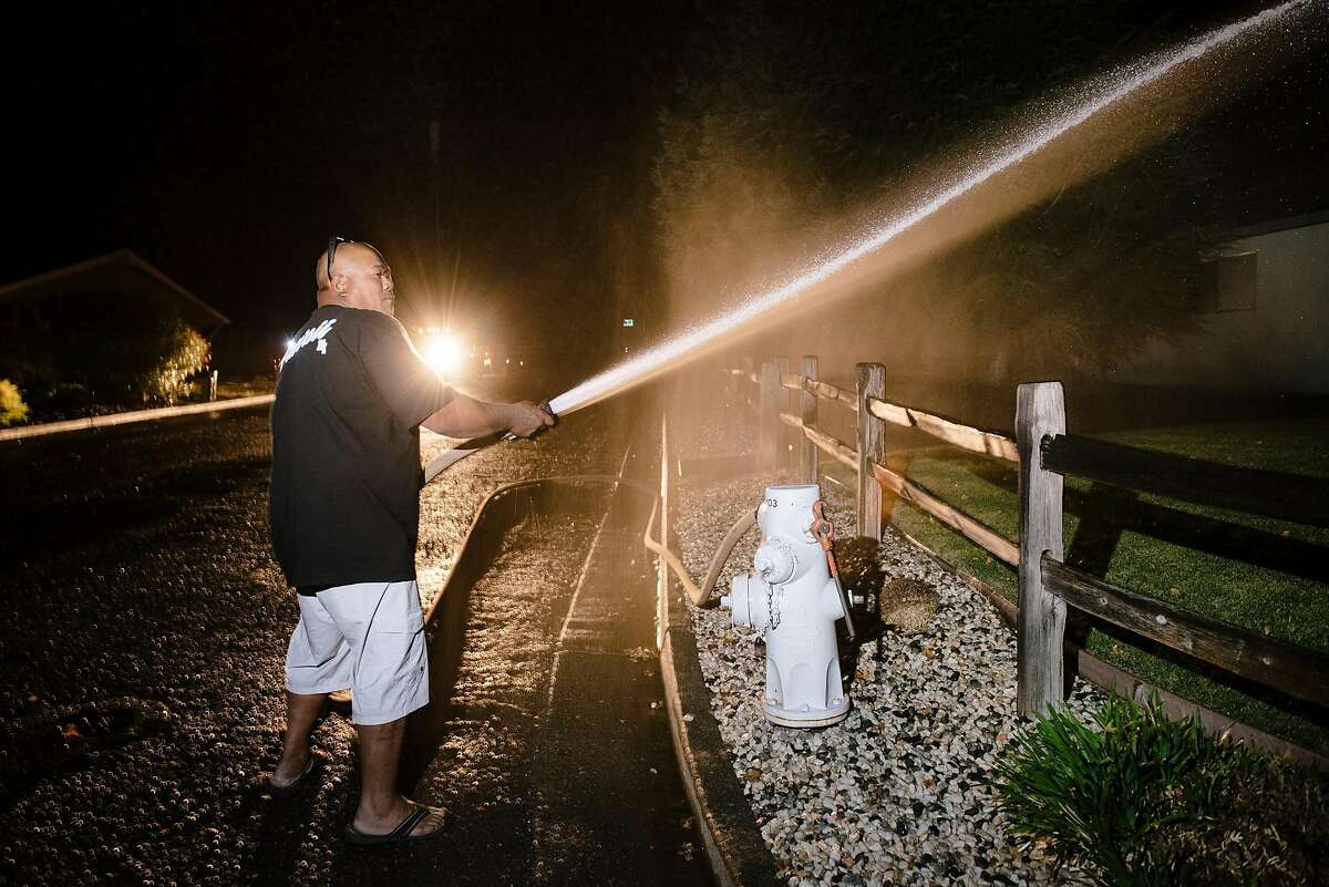 Cliff Nakamura uses his fire hose to wet down his neighbors house before evacuating his own home in Larkfield, California, on Saturday, Oct. 26, 2019.