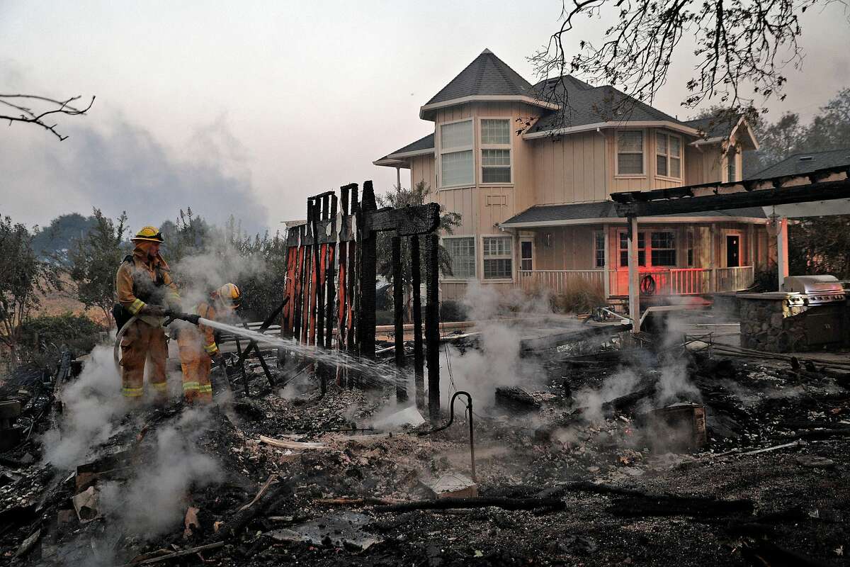 Firefighters extinguish hot spots in an out builiding that burned next to a house that was spared on Chalk Hill Road as the Kincade Fire burns outside Healdsburg, Calif., on Sunday, October 27, 2019.