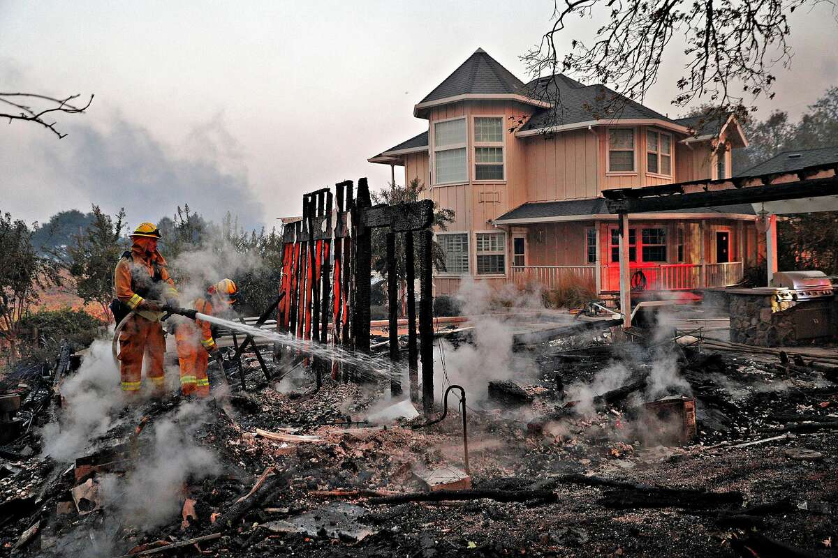 Firefighters extinguish hot spots in an out builiding that burned next to a house that was spared on Chalk Hill Road as the Kincade Fire burns outside Healdsburg, Calif., on Sunday, October 27, 2019.