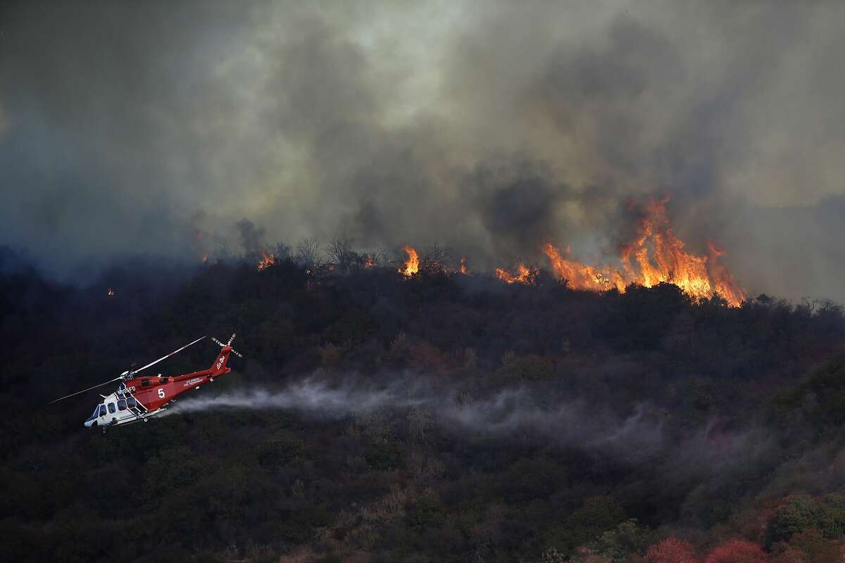 A wildfire called the Getty Fire burns a ridge top as a water-dropping helicopter flies by on Mandeville Canyon Monday, Oct. 28, 2019, in Los Angeles. (AP Photo/Marcio Jose Sanchez)