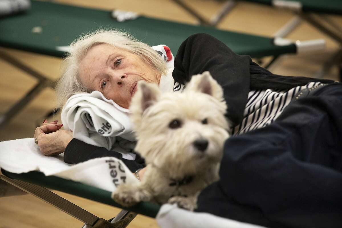 In this Sunday, Oct. 27, 2019, photo, Patti Hewitt rests on a cot with her dog at a Red Cross shelter set up for wildfire evacuees at the Sonoma County Fairgrounds in Santa Rosa, Calif., after evacuating her Santa Rosa home in the morning. The Red Cross established the shelter for evacuees with pets at the Sonoma County Fairgrounds. (John Burgess/The Press Democrat via AP)