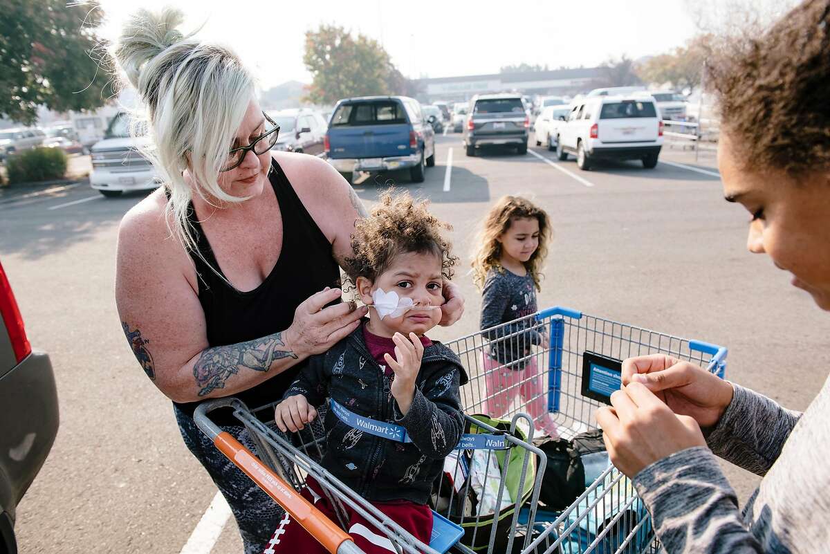 Santa Rosa evacuee Jodi Brock, adjusts the oxygen supply for her son True Brock, 2 years old, who has a congenital heart defect, as she visits Walmart with her family, including Khaleesi Brock, center and Malakai Brock, right, to buy air filter masks and special formula for True, in Rohnert Park, California, on Monday, Oct. 28, 2019.