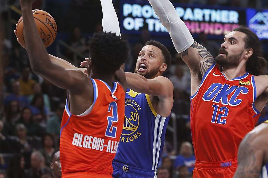 Golden State Warriors guard Stephen Curry (30) goes to the basket between Oklahoma City Thunder guard Shai Gilgeous-Alexander (2) and center Steven Adams (12) in the first half of an NBA basketball game Sunday, Oct. 27, 2019, in Oklahoma City. (AP Photo/Sue Ogrocki)