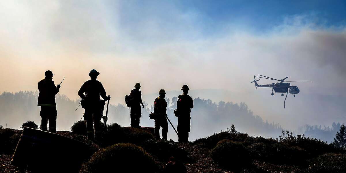 Firefighters watch as a helicopter drops water over the Kincade Fire near Ida Clayton Road in Calistoga, California, on Tuesday, Oct. 29, 2019.