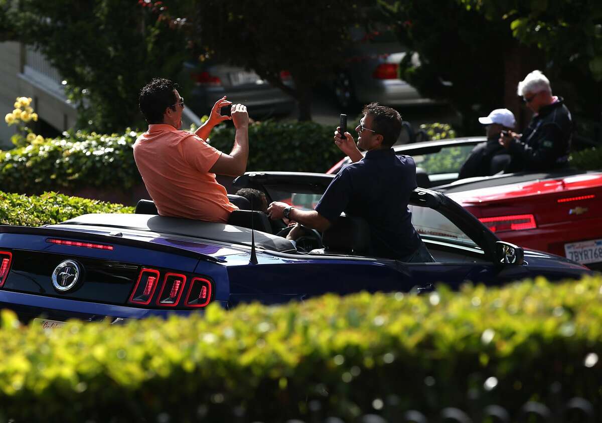 Tourists take pictures while driving down Lombard Street n San Francisco.